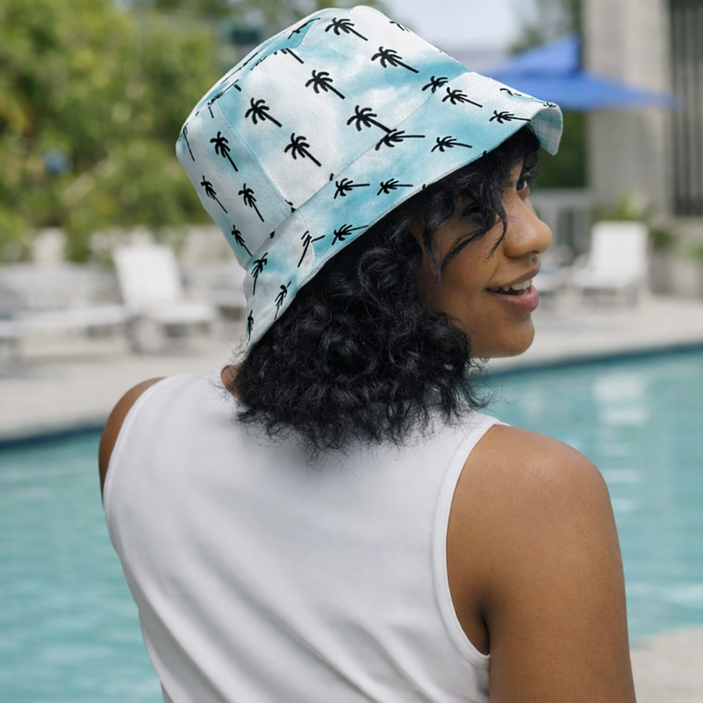 Woman wearing a Valley Girls Club bucket hat with palm tree pattern by a pool