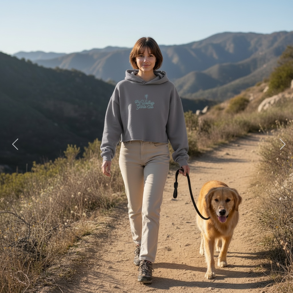 Woman walking a dog on a trail with mountains in the background wearing The Valley Girls Club Cropped Hoodie in Heather Grey